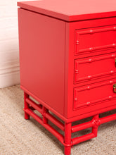 Load image into Gallery viewer, Image 12 of 21: A bright red three-drawer nightstand with a bamboo-inspired frame and gold-tone hardware, shown in a close-up indoor shot against a light wall and carpet.