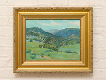 Load image into Gallery viewer, Original Felice Hrovat landscape painting with rolling green hills, mature trees and deep blue mountains in an ornate gold-tone frame.