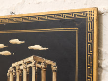 Load image into Gallery viewer, Close-up of a decorative wall art panel with a black background, gold Greek key border, and a classical column scene with cream clouds, mounted against a white textured wall.
