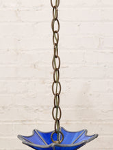 Load image into Gallery viewer, A vintage-style pendant light with a cobalt blue glass bowl and a weathered bronze metal chain, shown hanging against a white brick wall.