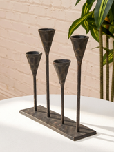 Load image into Gallery viewer, Three-tone metal cone candle holders on a rectangular base, displayed on a white table against a beige brick wall with a green plant in the background.