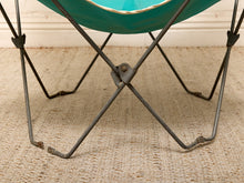 Load image into Gallery viewer, Close-up of a butterfly-style chair with a teal seat and a dark metal frame, shown on a woven beige rug against a white wall.
