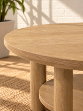 Load image into Gallery viewer, Image 5 of 5: Vito round coffee table in Sunwashed Oak with sculpted legs, circular lower shelf, and natural wood-grain finish