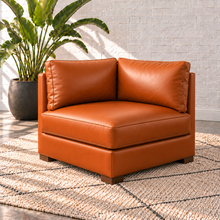 Load image into Gallery viewer, Image 9 of 14: Simulated Hollis 40-inch square corner module in Mont Blanc Caramel leather, with perpendicular backrests and two open connecting sides, styled with an ivory rug and bird-of-paradise plant.