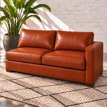 Load image into Gallery viewer, Image 14 of 14: Simulated Hollis 67-inch right-arm condo sofa in Mont Blanc Caramel leather with two seat cushions, two back cushions and open left side, styled with an ivory rug and bird-of-paradise plant.