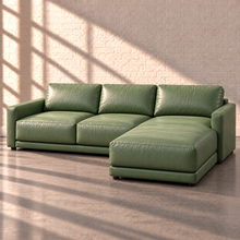 Load image into Gallery viewer, Image 2 of 18: Simulated Orinda two-piece leather sectional with a left-arm two-seat sofa and right-arm chaise in Sequoia Rainforest sage green leather, shown without accent pillows in the Sunbeam white brick setting.