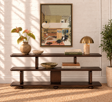Load image into Gallery viewer, A dark brown wooden console shelf with three tiers, styled with a vase of green leaves, bowls, books, and a brass lamp, set against a white brick wall with a framed picture and a potted plant.
