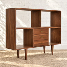 Load image into Gallery viewer, Mid-century modern wooden storage cabinet with three drawers and open shelving, shown against a white brick wall on a woven rug.
