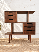 Load image into Gallery viewer, Mid-century modern wooden console table with three drawers on the left, three drawers on the right, open shelving, and tapered legs, set against a white brick wall and woven rug.

