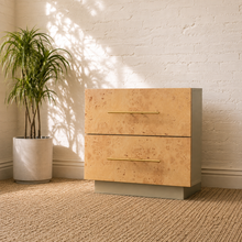 Load image into Gallery viewer, Modern two-drawer nightstand with light burl wood fronts, white top and sides, long brass-tone pulls and recessed plinth base.
