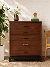 Load image into Gallery viewer, Vintage mid-century walnut highboy dresser with five drawers, brass-tone pulls, slim metallic trim and dark plinth base.
