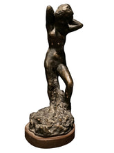 Load image into Gallery viewer, Pierre Bonnard Bronze-finished sculpture of a nude female figure standing on a textured rock base with a round wooden pedestal, photographed against a dark textured wall.
