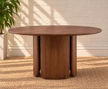 Load image into Gallery viewer, Amari round dining table in natural brown Mindi wood with sculptural rounded column pedestal base and visible wood grain.

