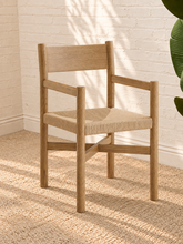 Load image into Gallery viewer, Amelie natural solid oak dining armchair with woven paper-rope seat, curved wood backrest, slim armrests, and X-shaped stretcher
