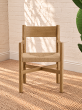 Load image into Gallery viewer, Amelie natural solid oak dining armchair with woven paper-rope seat, curved wood backrest, slim armrests, and X-shaped stretcher
