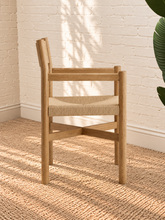 Load image into Gallery viewer, Amelie natural solid oak dining armchair with woven paper-rope seat, curved wood backrest, slim armrests, and X-shaped stretcher
