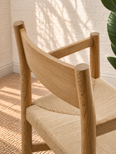 Load image into Gallery viewer, Amelie natural solid oak dining armchair with woven paper-rope seat, curved wood backrest, slim armrests, and X-shaped stretcher
