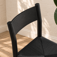 Load image into Gallery viewer, Amelie charcoal solid oak dining chair with woven paper-rope seat, curved wood backrest, rounded legs, and X-shaped stretcher
