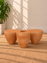 Load image into Gallery viewer, Aster sculptural coffee table in Amber fiber-reinforced concrete with four rounded pedestal forms and a distinctive central tabletop opening.
