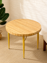 Load image into Gallery viewer, Vintage round Formica dining table with wood-grain pattern, center leaf seam, and mustard yellow tapered metal legs.
