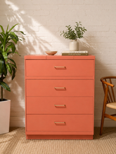 Load image into Gallery viewer, Coral pink four-drawer tall dresser with clean modern lines, brass bar pulls, and a plinth base.
