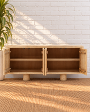 Load image into Gallery viewer, Cailah natural light reclaimed pine wood credenza with four cabinet doors, subtle wood grain, interior shelving, and rounded pedestal legs.

