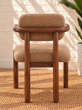 Load image into Gallery viewer, Caroline dining chair upholstered in toffee brown burlap fabric with curved wraparound back, rounded arms, and Mindi wood legs.
