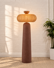 Load image into Gallery viewer, Chandria floor lamp with tall tapered brown fiber cement base, rounded woven rattan shade, and faceted decorative finial.
