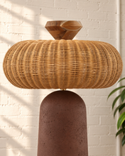 Load image into Gallery viewer, Chandria floor lamp with tall tapered brown fiber cement base, rounded woven rattan shade, and faceted decorative finial.
