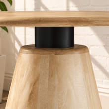 Load image into Gallery viewer, A natural light wood table base with a tapered conical shape and a black metal pedestal joint, shown in a bright room on a woven rug.
