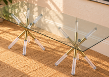 Load image into Gallery viewer, Flavia rectangular glass dining table with tempered glass top and sculptural X-shaped base in gold metal and clear acrylic.
