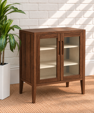 Load image into Gallery viewer, Hilda warm walnut bar cabinet with two tempered glass doors, recessed finger pulls, light interior shelves, and tapered wood legs
