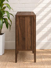 Load image into Gallery viewer, Hilda warm walnut bar cabinet with two tempered glass doors, recessed finger pulls, light interior shelves, and tapered wood legs

