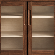 Load image into Gallery viewer, Hilda warm walnut bar cabinet with two tempered glass doors, recessed finger pulls, light interior shelves, and tapered wood legs
