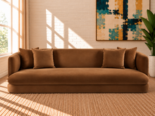 Load image into Gallery viewer, Isabelle sofa in Caramel 460 GSM velvet with curved arms, rounded base, plush seat, and coordinating throw pillows.
