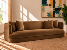 Load image into Gallery viewer, Isabelle sofa in Caramel 460 GSM velvet with curved arms, rounded base, plush seat, and coordinating throw pillows.
