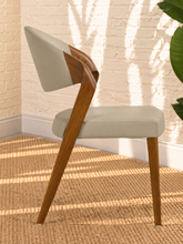 Load image into Gallery viewer, Kori warm greige leatherette dining chair with curved upholstered back and walnut-finished solid ash wood frame.
