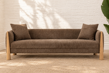 Load image into Gallery viewer, Lexi three-seat sofa upholstered in textured taupe brown fabric with exposed solid wood legs, square arms, and two matching toss pillows.
