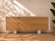 Load image into Gallery viewer, Marlee four-door credenza with natural oak veneer doors, faux travertine surround, interior shelving, and two rounded pedestal legs.
