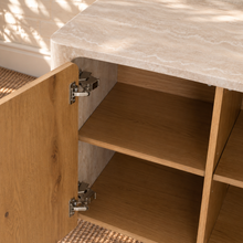 Load image into Gallery viewer, Marlee four-door credenza with natural oak veneer doors, faux travertine surround, interior shelving, and two rounded pedestal legs.
