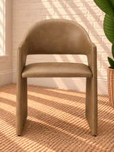 Load image into Gallery viewer, Nora tan vegan leather dining armchair with curved barrel back, open-back detail, padded seat, and wide upholstered sides
