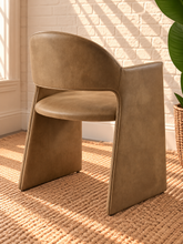 Load image into Gallery viewer, Nora tan vegan leather dining armchair with curved barrel back, open-back detail, padded seat, and wide upholstered sides
