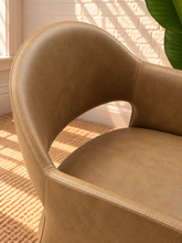 Load image into Gallery viewer, Nora tan vegan leather dining armchair with curved barrel back, open-back detail, padded seat, and wide upholstered sides
