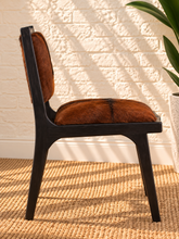 Load image into Gallery viewer, Odessa dining chair in natural chestnut genuine goat hide with a tall upholstered back, rounded seat, and exposed teak wood frame.
