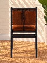 Load image into Gallery viewer, Odessa dining chair in natural chestnut genuine goat hide with a tall upholstered back, rounded seat, and exposed teak wood frame.
