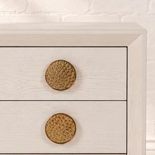 Load image into Gallery viewer, Pair of Phoebe three-drawer nightstands in cream white ash veneer with textured round golden metal handles and recessed plinth bases.

