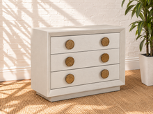 Load image into Gallery viewer, Phoebe three-drawer nightstand in cream white ash veneer with six round textured golden metal handles and recessed plinth base.
