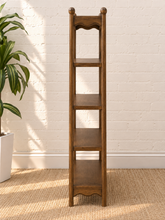 Load image into Gallery viewer, Image 4 of 5: A tall, narrow wooden shelving unit with four tiers stands against a white brick wall on a woven jute rug, with a potted green plant visible on the left.

