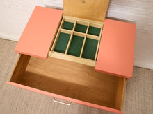Load image into Gallery viewer, A coral pink and light wood drawer organizer with an open bottom drawer and a hinged top section that opens into a six-compartment organizer tray with dark green felt lining, set against a white brick wall and beige carpet.
