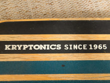 Load image into Gallery viewer, A close-up of a striped wooden box or case with black, light wood, and teal stripes, featuring the text 'KRYPTONICS SINCE 1965' in white on a black stripe. A woven beige fabric is visible in the background.
